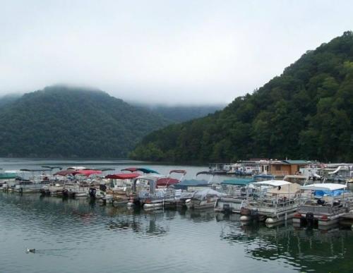 A serene lake scene with boats docked at a marina, surrounded by misty mountains and lush greenery.