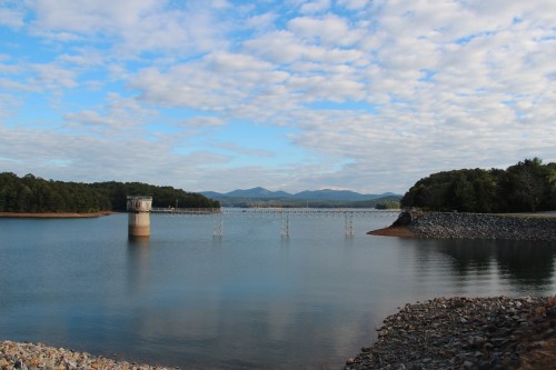A serene lake scene with a tower, bridge, and mountains under a partly cloudy sky.