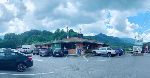 A restaurant with a brick exterior surrounded by cars, set against a backdrop of mountains and cloudy skies.