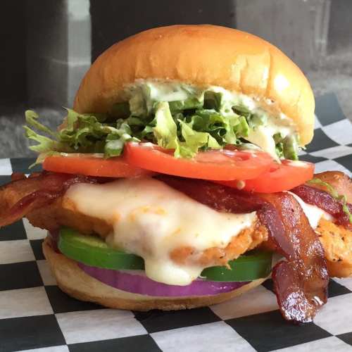 A delicious chicken sandwich with bacon, lettuce, tomato, green pepper, onion, and creamy sauce on a soft bun.
