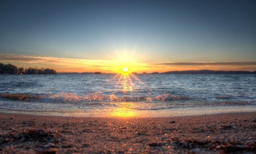 A serene beach at sunset, with waves gently lapping at the shore and a vibrant sun setting over the horizon.