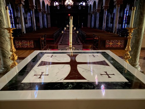 A view of an ornate altar with a cross design, surrounded by candle holders, inside a grand church.