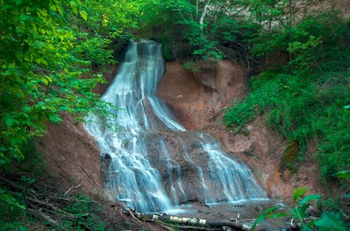 A serene waterfall cascading down a rocky slope, surrounded by lush green foliage and trees.