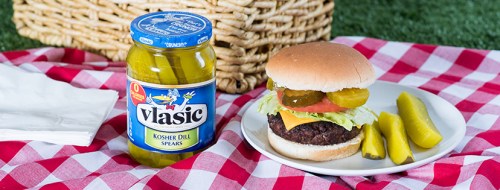 A plate with a burger topped with lettuce, tomato, and pickles, alongside a jar of Vlasic Kosher Dill Spears and pickles.