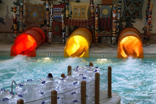 Three colorful water slides lead into a pool, with a person in an inner tube floating nearby.