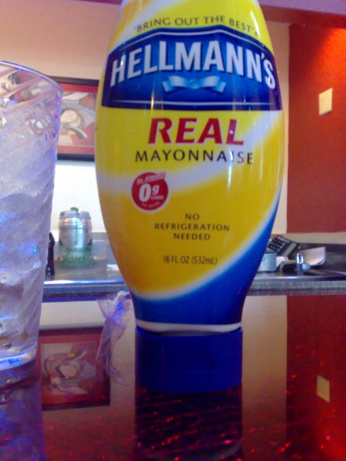 A bottle of Hellmann's Real Mayonnaise on a table, next to a glass of ice.