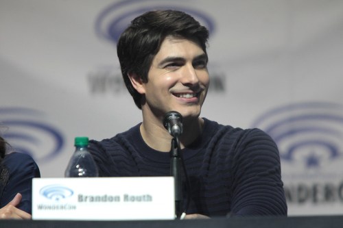 A smiling man at a panel discussion, sitting behind a microphone with a water bottle nearby.