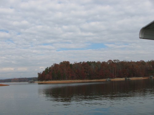 A serene lake scene with autumn-colored trees lining the shore under a cloudy sky.