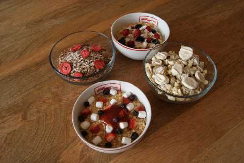 Four bowls of cereal with various toppings, including fruits and marshmallows, on a wooden surface.