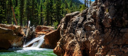 A serene landscape featuring a flowing waterfall surrounded by lush green trees and rocky terrain.