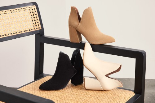Three stylish ankle boots in beige, black, and white displayed on a modern chair with a woven seat.