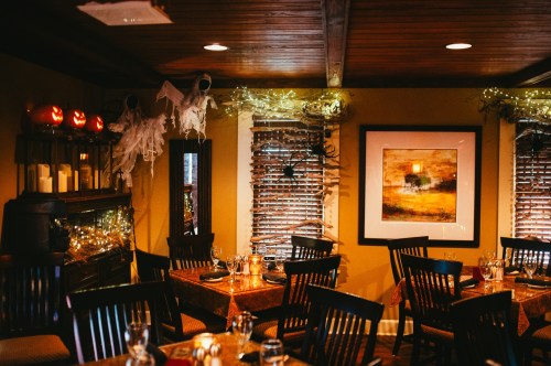 Cozy restaurant interior decorated for Halloween with pumpkins, ghosts, and warm lighting.