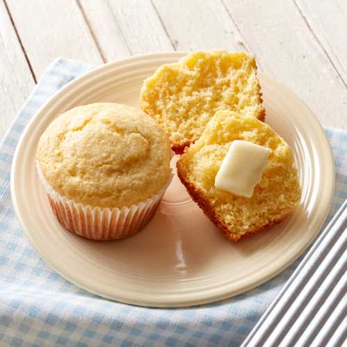 A plate with a golden corn muffin, one whole and one cut in half, topped with a pat of butter.