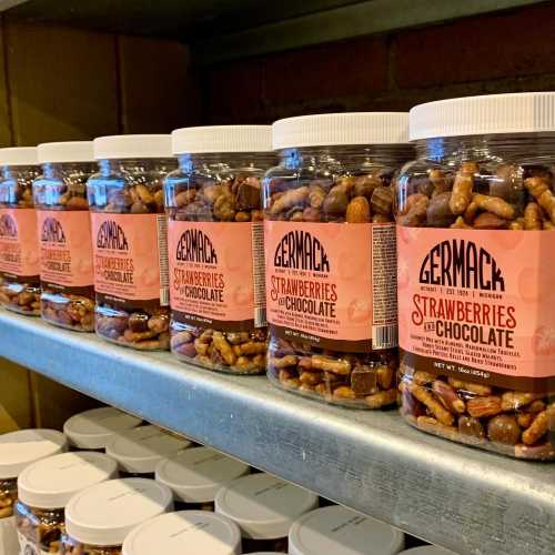 Jars of Germack's chocolate-covered strawberries and pretzels lined up on a shelf.