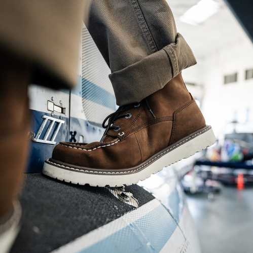 A close-up of a brown boot resting on a surface, with a blurred background of an indoor space.