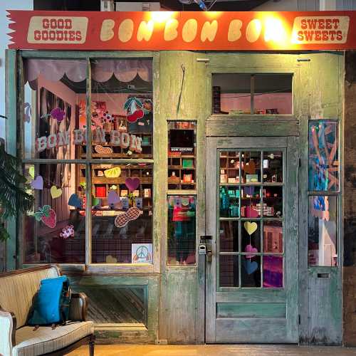 Colorful storefront of "Bon Bon Bon" featuring a vintage green door and window displays of sweets and decorations.