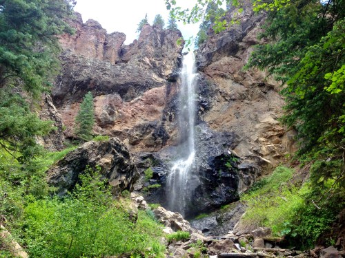 A waterfall cascading down rocky cliffs, surrounded by lush greenery and trees in a natural setting.