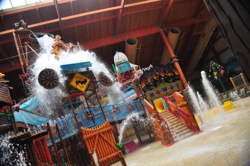 A colorful indoor water park with a large water play structure, featuring slides and water splashes.
