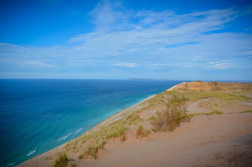 A scenic view of a sandy shoreline meeting a calm blue ocean under a clear sky.