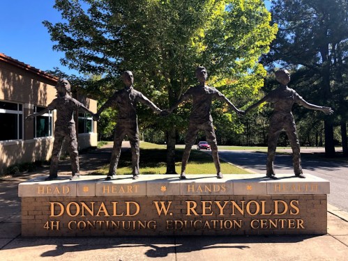 Sculpture of three children holding hands, with a sign for the Donald W. Reynolds 4H Continuing Education Center.