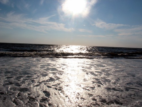 A sunlit ocean scene with gentle waves and a bright sky, reflecting sunlight on the water's surface.