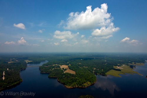 Aerial view of a lush landscape with lakes, forests, and scattered clouds under a blue sky.