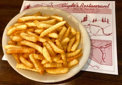 A plate of golden crinkle-cut fries on a table with a restaurant map in the background.