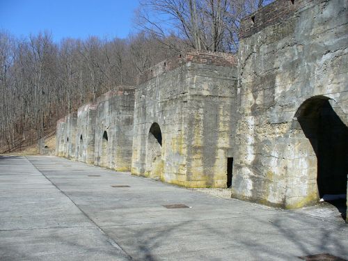 Abandoned stone structures with arched openings, set against a backdrop of bare trees and a clear blue sky.