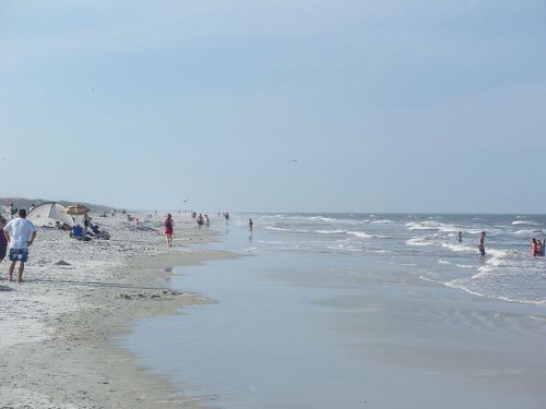 A sandy beach with people walking, playing, and relaxing near the water under a clear blue sky.