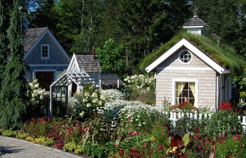 Charming garden scene with two quaint houses surrounded by vibrant flowers and lush greenery.