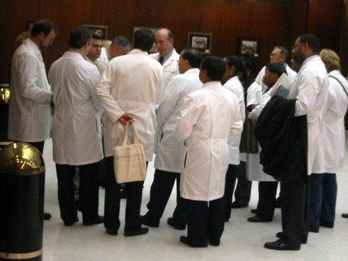 A group of doctors in white lab coats gathered in a hallway, engaged in discussion.
