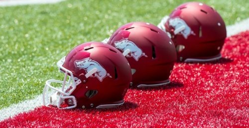 Three red football helmets with a white hog logo lined up on a red turf field.