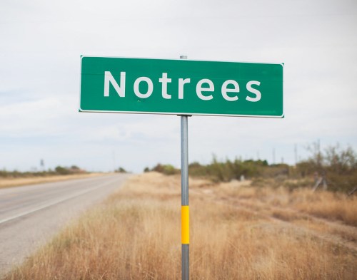 A green road sign reading "Notrees" stands beside a highway, with dry grass and a cloudy sky in the background.