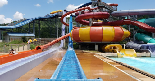 A vibrant water park featuring multiple slides, a large inflatable, and a pool under a clear blue sky.