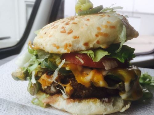 A close-up of a loaded burger with lettuce, tomato, cheese, and a sesame seed bun, resting on a napkin.