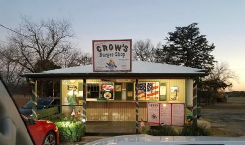 A small burger shop with a sign reading "Crow's Burger Shop," featuring outdoor seating and American flags.