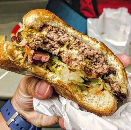 A close-up of a hand holding a juicy hamburger with layers of meat, cheese, and fresh toppings in a toasted bun.