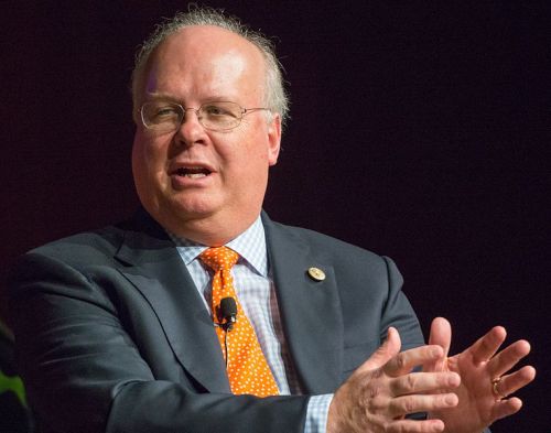 A man in a suit with glasses speaks passionately at a podium, gesturing with his hands.