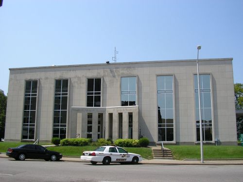 Modern building with large glass windows, steps leading to the entrance, and a police car parked in front.