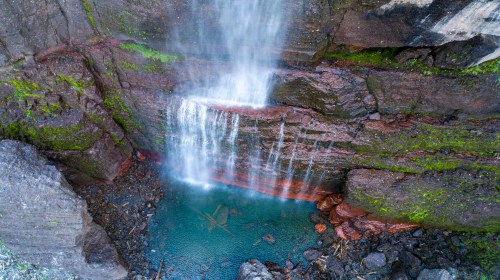 A serene waterfall cascading over rocky cliffs into a clear blue pool surrounded by moss and stones.