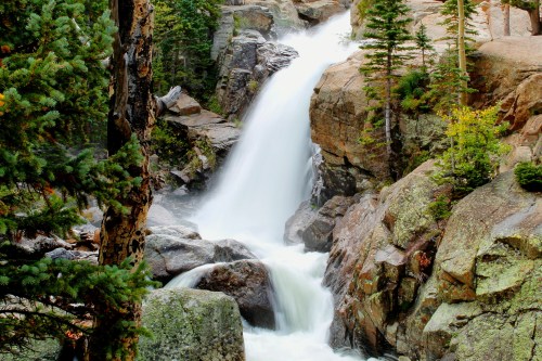 A serene waterfall cascading over rocky terrain, surrounded by lush green trees and autumn foliage.