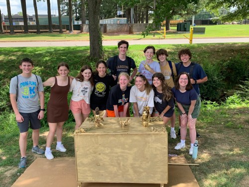 A group of diverse young adults poses together around a decorated wooden table outdoors.