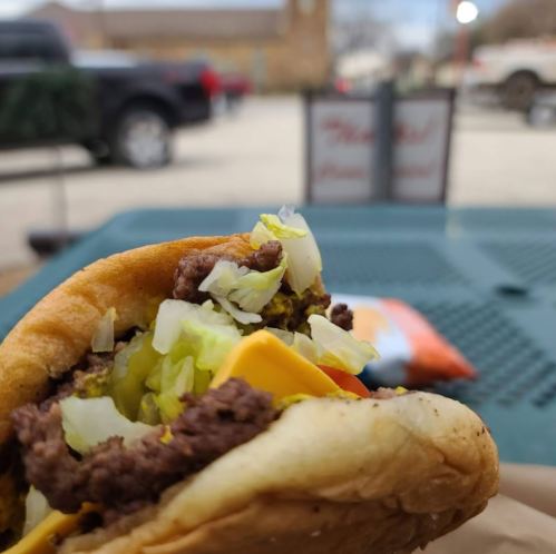 A close-up of a cheeseburger with lettuce and mustard, set against a blurred outdoor background.