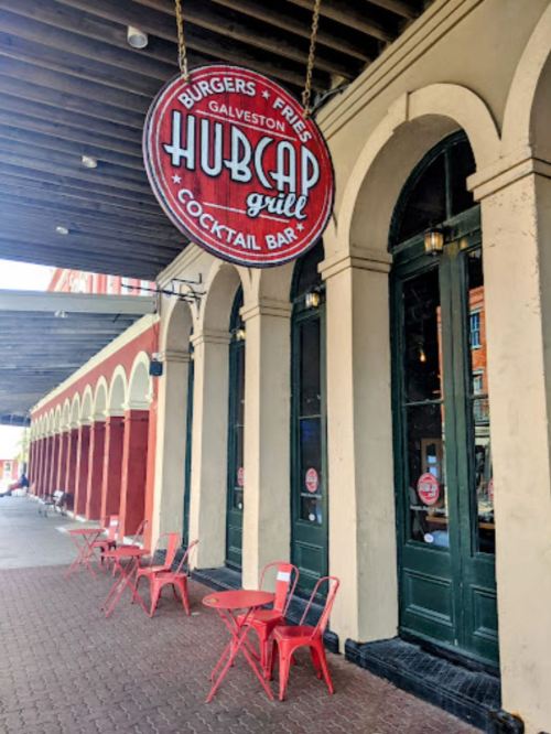 Sign for Hubcap Grill, a burger and cocktail bar, with outdoor seating and arched doorways in Galveston.