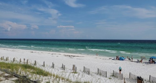 A serene beach scene with white sand, turquoise waves, and people enjoying the sun under blue skies.