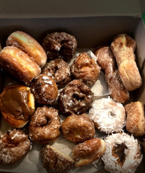 A box filled with a variety of donuts, including glazed, chocolate-covered, and coconut-topped options.