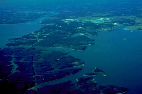 Aerial view of a river winding through green landscapes and islands, with a distant town visible along the shore.