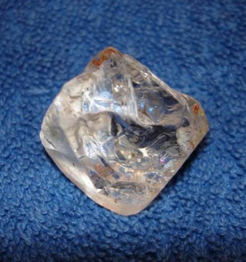 A clear, irregularly shaped crystal resting on a blue textured surface.