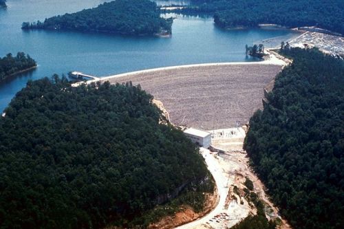 Aerial view of a dam surrounded by lush green forests and a serene blue lake.