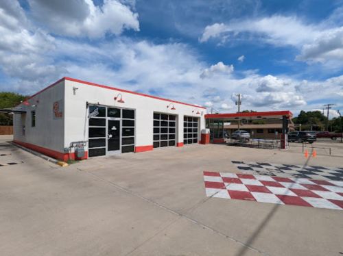 A white building with red accents, featuring large garage doors and a checkered pavement, under a blue sky with clouds.